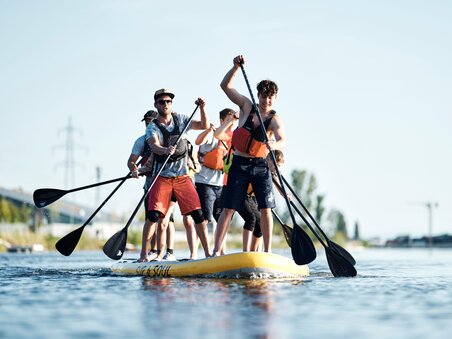 Gruppe von Menschen paddelt auf einem großen SUP im Wasser. | © Stadtstrand Graz - Stefan Leitner