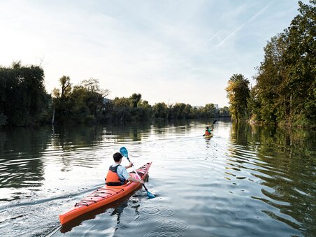 Zwei Personen im Kajak paddeln auf der ruhigen Mur umgeben von Bäumen. | © Stadtstrand Graz - Stefan Leitner