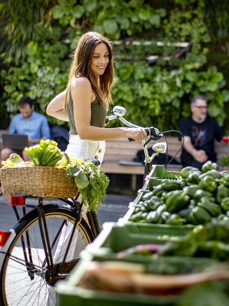 Donna in bicicletta acquista verdure fresche al mercato Kaiser Josef di Graz. | © Graz Tourismus - Tom Lamm