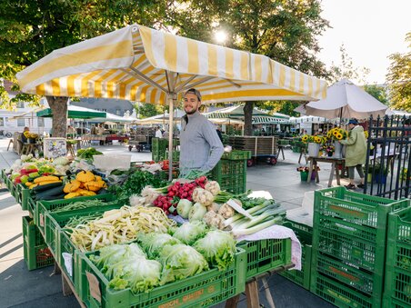 Scena di mercato vivace con verdure fresche e venditore a Graz. | © Graz Tourismus - Mias Photoart