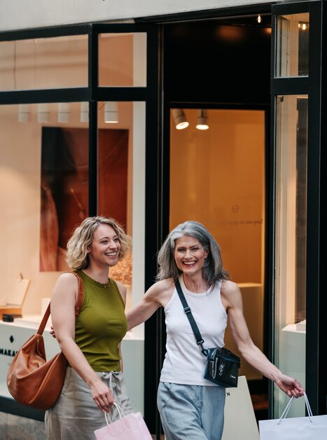 Zwei Frauen lächeln und tragen Einkaufstaschen in Graz. | © Graz Tourismus - Mias Photoart