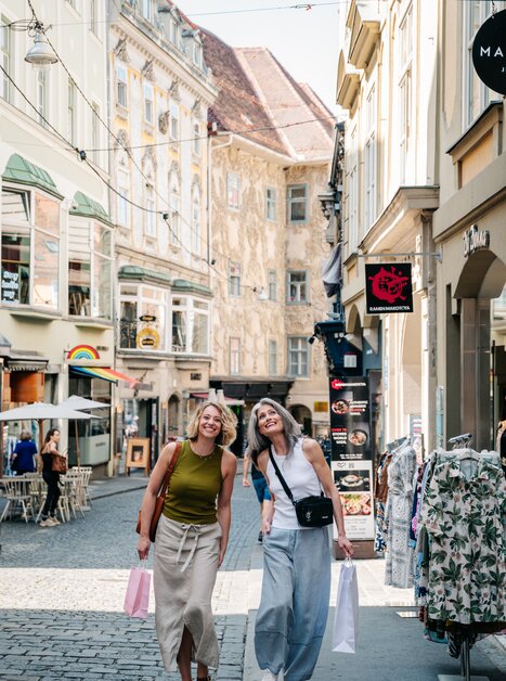 Zwei Frauen lächeln beim Einkaufen in Graz, mit Tüten in der Hand. | © Graz Tourismus - Mias Photoart