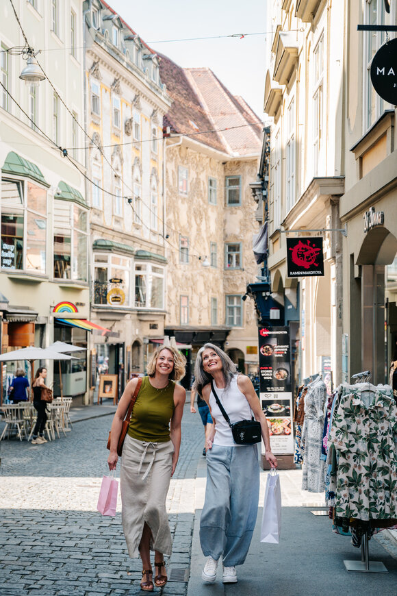 Zwei Frauen lächeln beim Einkaufen in Graz, mit Tüten in der Hand. | © Graz Tourismus - Mias Photoart