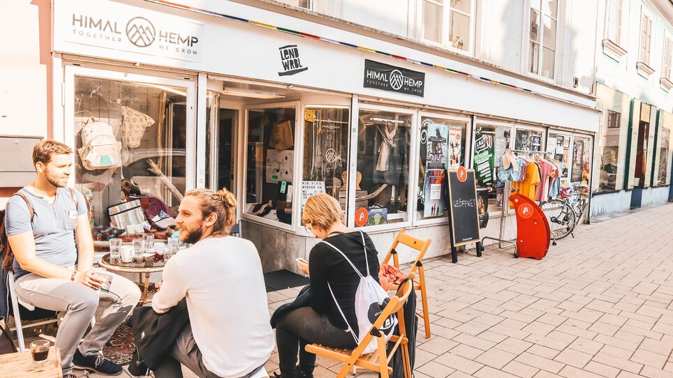 Three people are sitting in front of a shop in the Lendviertel neighbourhood in Graz. | © Janet Newenham - Journalist On The Run