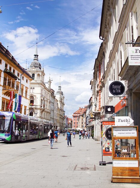 View of a busy street in Graz with shops and tram. | © sFachl