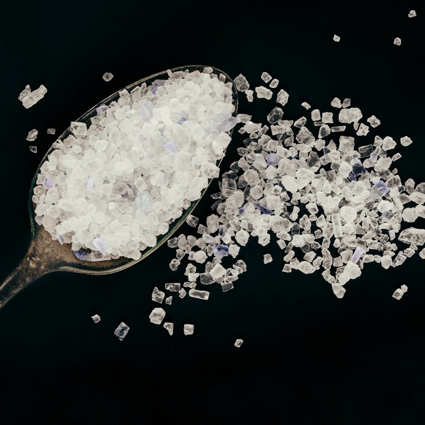 Ein Löffel voller Meersalz, das teilweise auf die dunkle Oberfläche fällt. | © Lupi Spuma