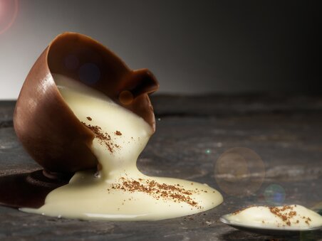Una tazza di cioccolato rovesciata con crema che fuoriesce su una superficie di legno. | © Eckhards Confiserie