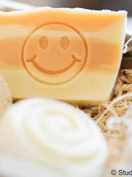 Bunte Seife mit einem lächelnden Gesicht und einer Spiralseife im Hintergrund. | © Studio Lou
