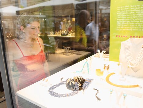 Una donna in un vestito rosso guarda affascinata i gioielli in una vetrina. | © Graz Tourismus - Harry Schiffer