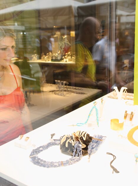 Eine Frau in einem roten Kleid schaut fasziniert auf Schmuck in einem Schaufenster. | © Graz Tourismus - Harry Schiffer