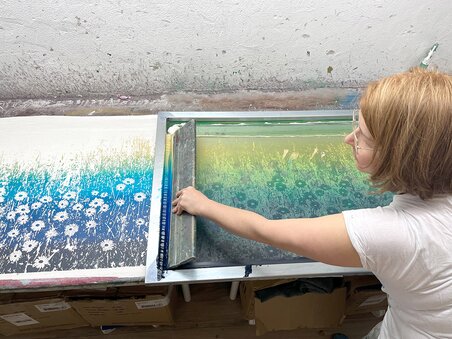 Eine Person arbeitet an einem Farbdruck im Atelier, umgeben von Kunstmaterialien. | © Peaces
