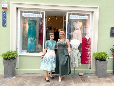 Due donne davanti a un atelier di abbigliamento a Graz, circondate da abiti e piante. | © Peaces