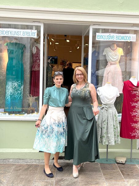 Zwei Frauen vor einem Kleideratelier in Graz, umgeben von Kleidern und Pflanzen. | © Peaces