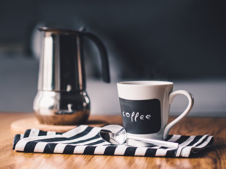 Eine Kaffeetasse steht neben einem Kaffeebereiter auf einem gestreiften Tuch. | © Pixabay
