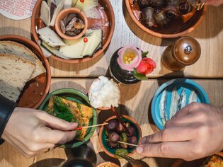 Tavolo pieno di tapas e bevande, mani che raggiungono gli snack. | © Cielo