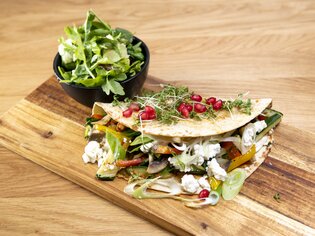 Quesadilla vegetariana servita su un tagliere di legno con insalata. | © Bistro Fino