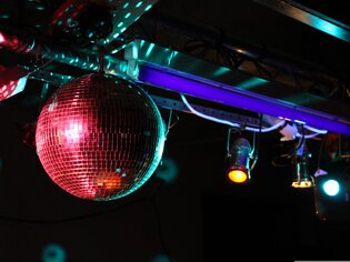 Eine glitzernde Discokugel hängt unter bunten Lichtern. | © Pixabay - manuelhauser