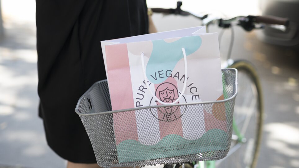 Eine Frau in schwarz steht neben einem Fahrrad mit einer Einkaufstasche im Korb. | © Eisperle - Stiefkind Fotografie