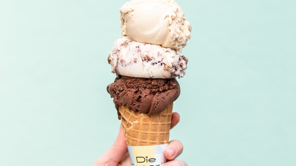 Eine schmackhafte Eistüte mit drei Kugeln Eis in verschiedenen Geschmacksrichtungen vor einem mintgrünen Hintergrund. | © Eisperle - Stiefkind Fotografie