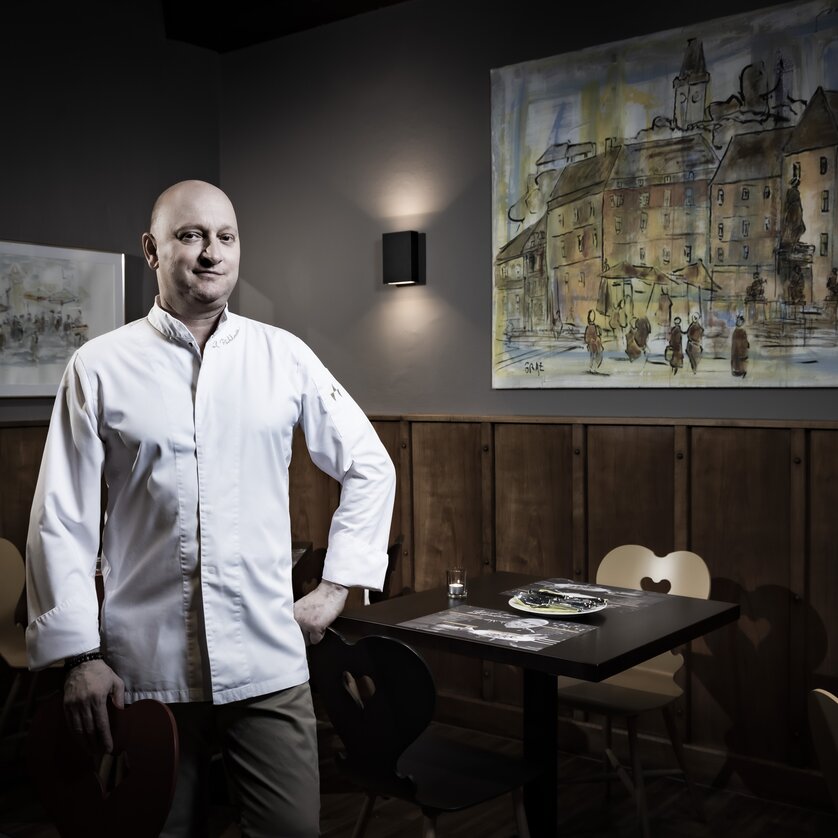 Ein Koch steht in einem Restaurant mit einem Gemälde im Hintergrund. | © Graz Tourismus - Werner Krug