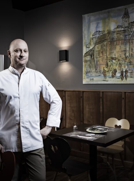 Ein Koch steht in einem Restaurant mit einem Gemälde im Hintergrund. | © Graz Tourismus - Werner Krug