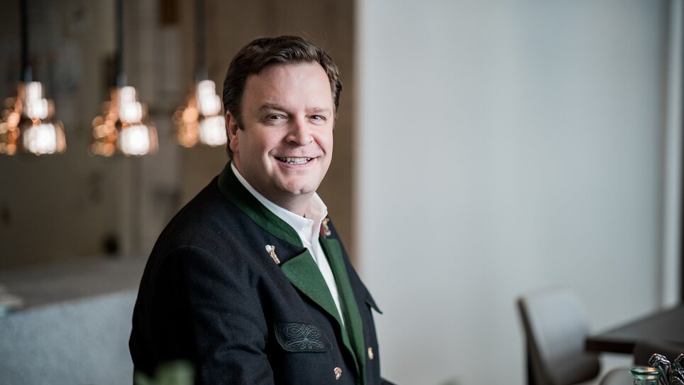 A man in traditional attire smiles at the table. Soft lighting in the background. | © Tina Szabo