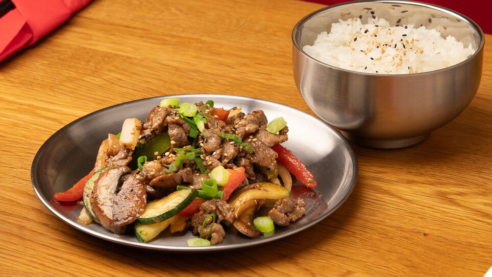 Ein Teller mit gebratenem Fleisch und Gemüse neben einer Schüssel Reis. | © Gogi KG