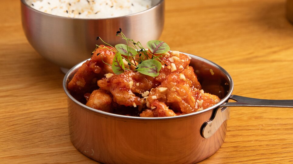 Ein silberner Behälter mit süßem Hähnchen und Reis, serviert auf einem Holztisch. | © Gogi KG