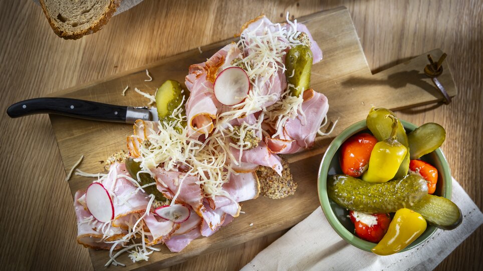 Un tagliere di legno con affettati, formaggio, cetrioli e un contorno di antipasti colorati. | © Kaiser Greissler - Werner Krug