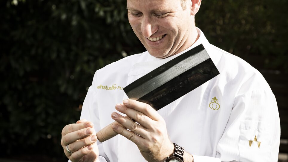 Un cuoco sorridente esamina un grande coltello da cucina. | © Werner Krug