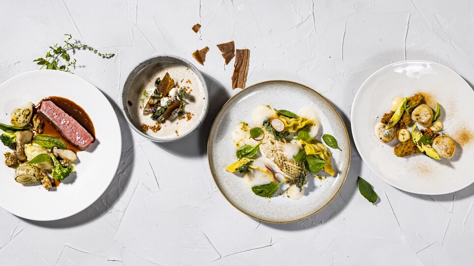 Vier kunstvoll angerichtete Teller mit verschiedenen Gerichten. | © Restaurant Schlossberg - Werner Krug