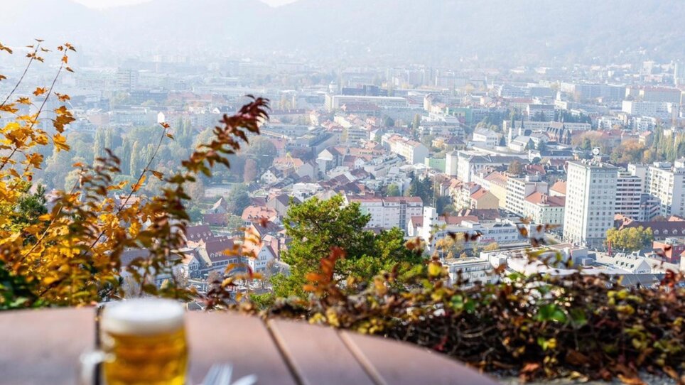 A round table with a glass of beer - in the background a view of the city of Graz. | © Restaurant Schlossberg