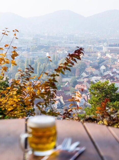 Ein runder Tisch mit einem Glas Bier - im Hintergrund Aussicht auf die Stadt Graz. | © Restaurant Schlossberg