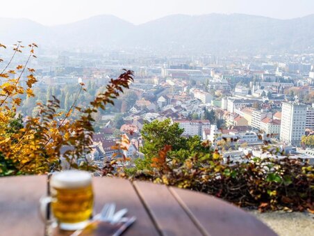 A round table with a glass of beer - in the background a view of the city of Graz. | © Restaurant Schlossberg