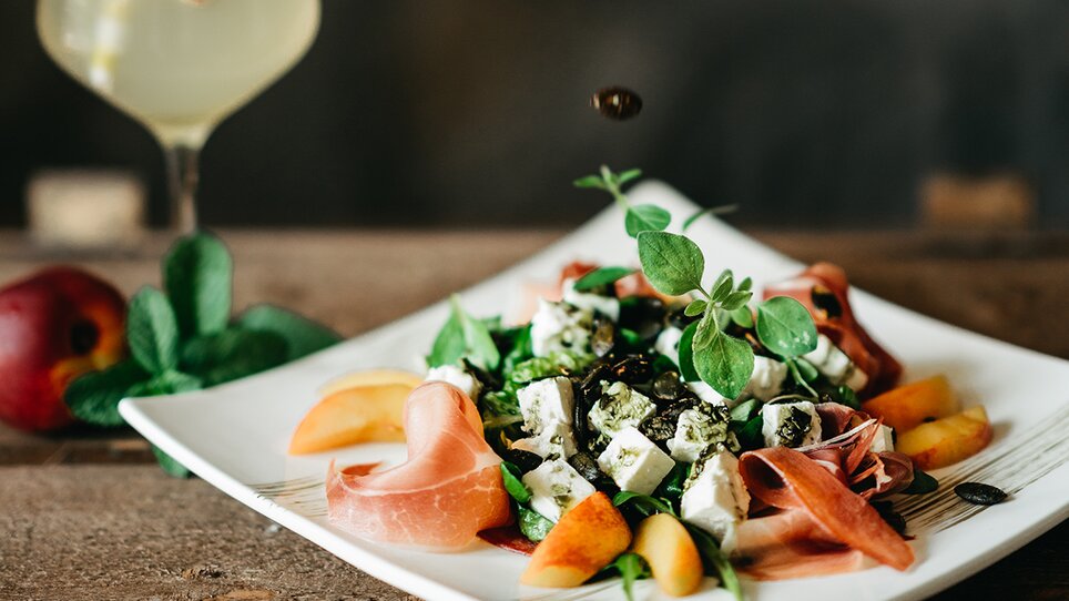 Fresh salad with dressing, a drink, and a hand adding ingredients. | © Julian Wallner