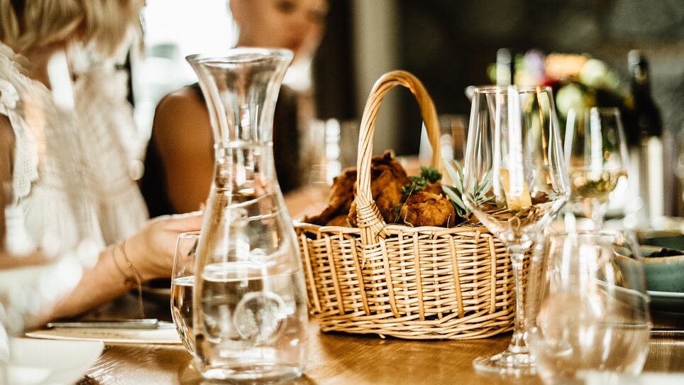 Beautifully laid table with glasses and a basket of fresh fried chicken in the Thorbauer inn. | © Julian Wallner