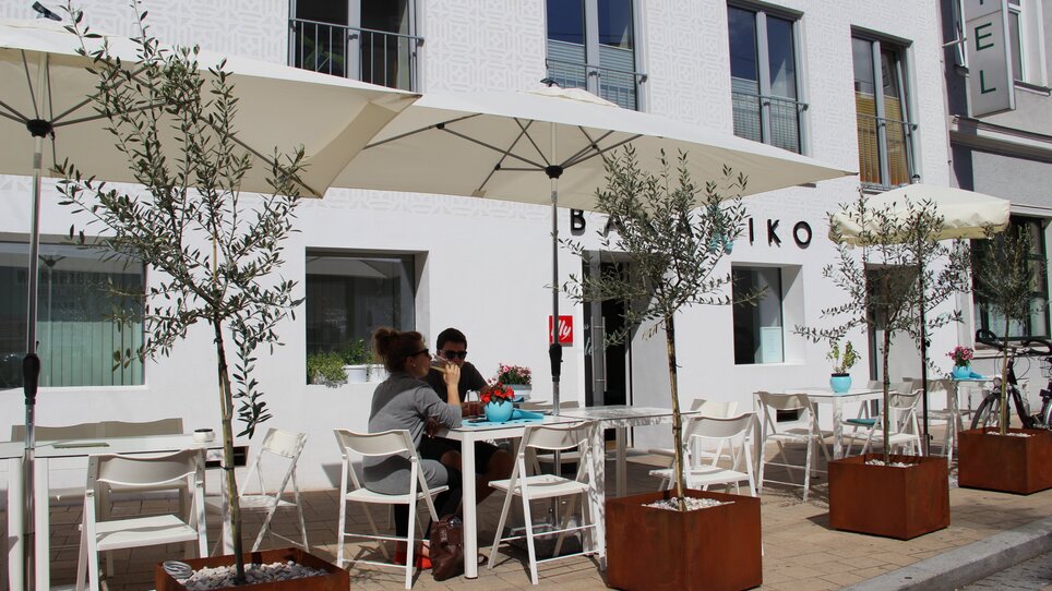 Freiluftbereich eines Restaurants mit Olivenbäumen und Sonnenschirmen in Graz. | © Bakaliko