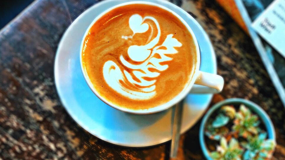 Ein köstlicher Kaffee mit Milchschaum in einer Tasse auf einem Holztisch. | © Beanery