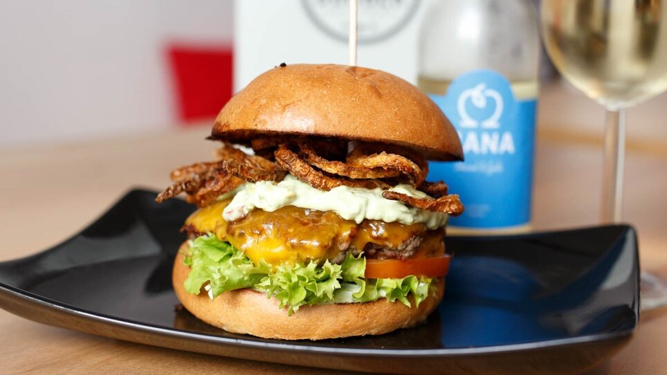 Juicy burger with cheese, lettuce, and onion rings on a plate. | © Burger Factory