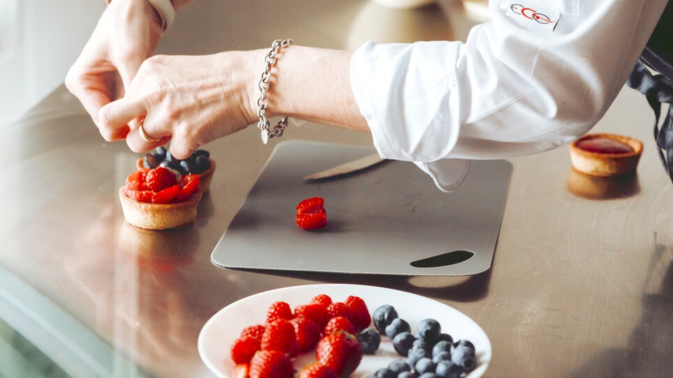 Eine Köchin dekoriert einen Kuchen mit frischen Beeren. | © Daniel_Stampfl