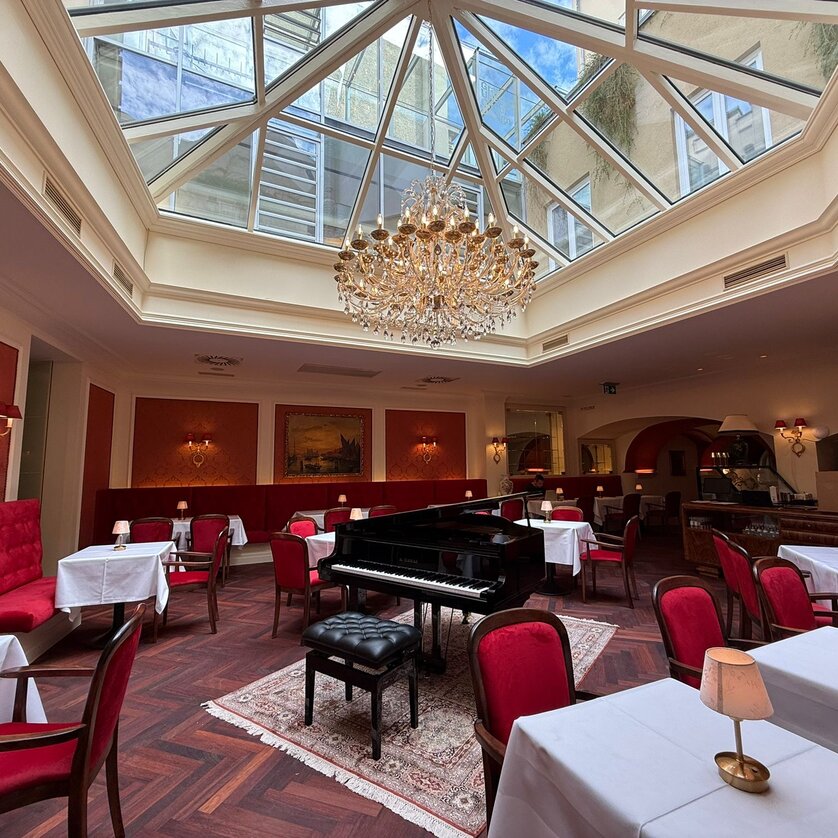 Caffè elegante con pianoforte, lampadario e tetto in vetro. | © Café Herzog