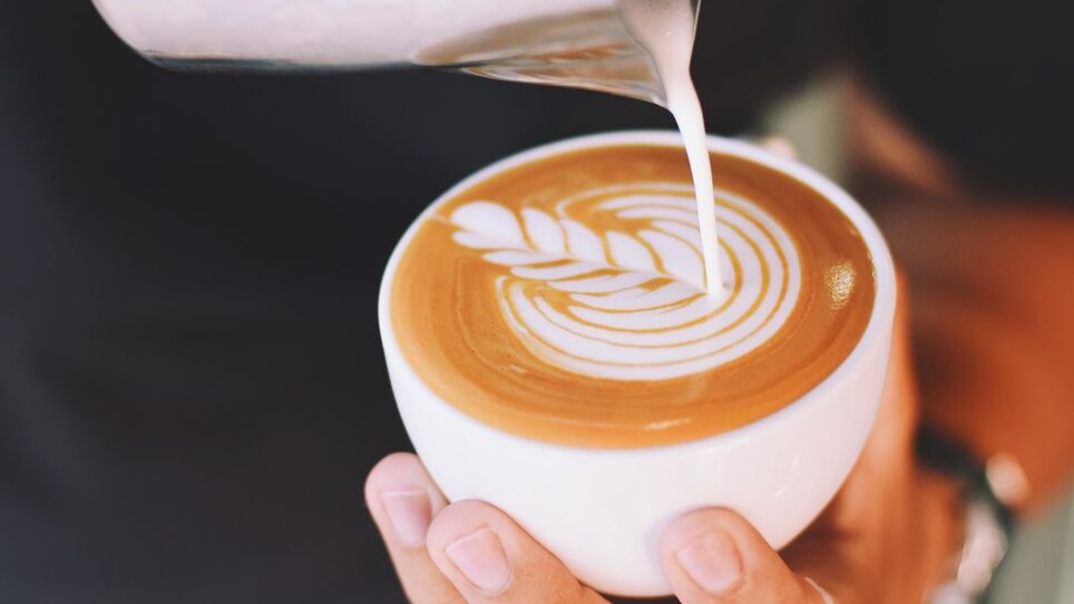Eine Person gießt Milch in eine Tasse mit Kaffee. | © Café Muhr