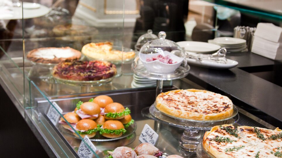 Delicacies displayed in a bar showcase, including cakes and croissants. | © Tageskaffee Freiblick 