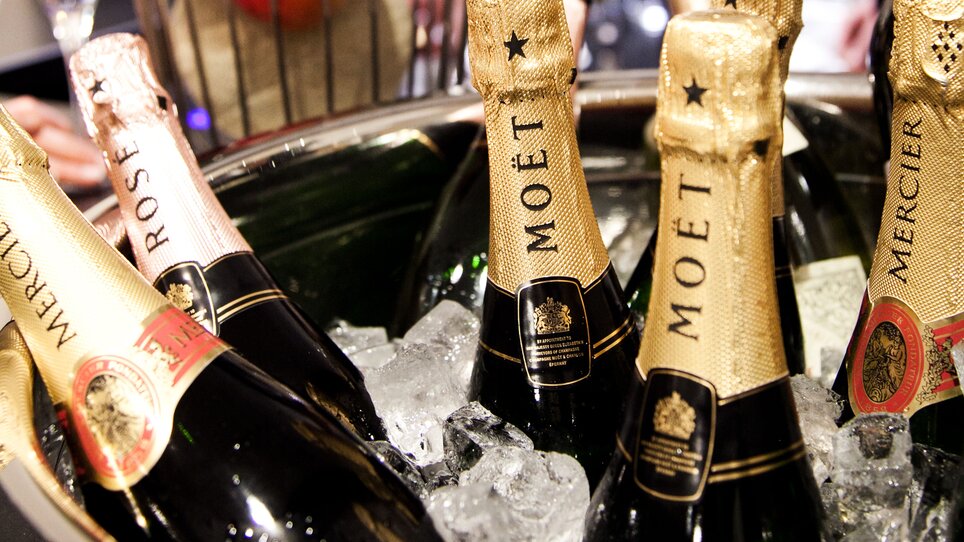 Champagne bottles in an ice bucket with fruits in the background. | © Tageskaffee Freiblick 