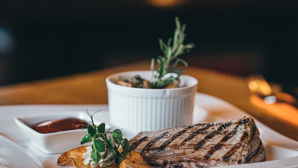 Grilled steak with sauces and sides served on a white plate. | © LevelUP
