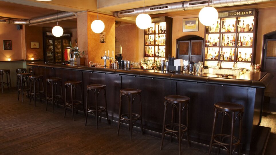 Bar accogliente con bancone in legno e grandi luci. | © cohibar