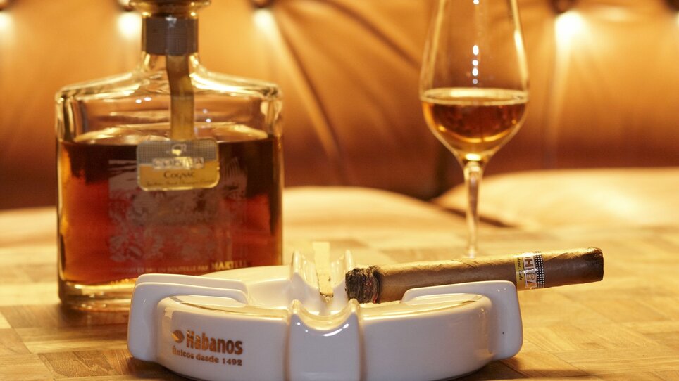 Whiskey, sigaro e bicchiere su un tavolo in un ambiente accogliente. | © cohibar