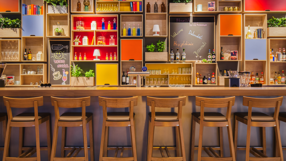 Modern bar with counter, colorful shelves, and drinks. | © IntercityHotel Graz