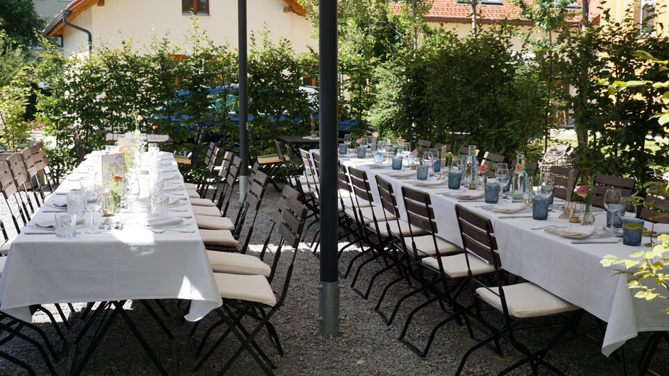 Una terrazza di giardino allestita con tavoli e sedie, pronta per mangiare. | © Das Lorenz
