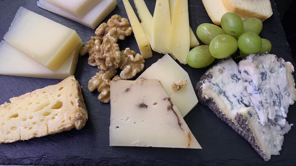 A cheese platter with walnuts and grapes on a black board. | © Nussbaumer